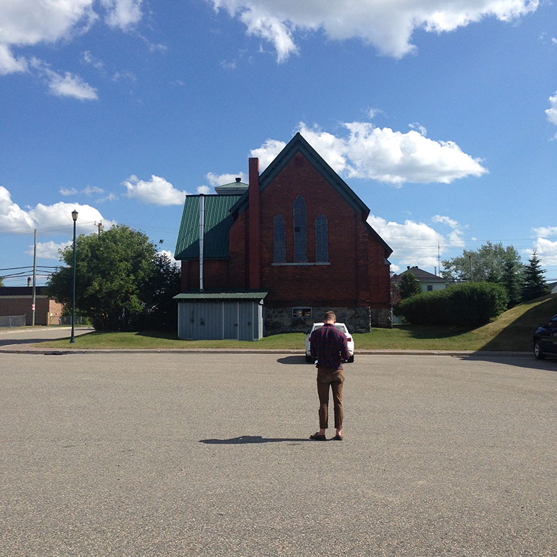 A man stands in an empty church parking lot looking at the church.